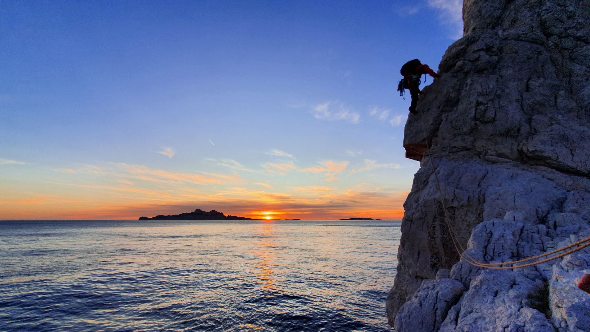 Grimpeur en tête sur une falaise au-dessus de la mer, au coucher du soleil